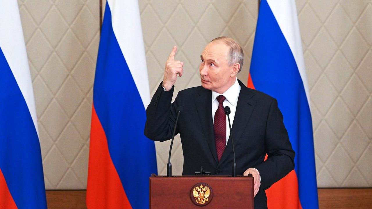 Russian President Vladimir Putin points his right index finger upwards and looks upwards too.