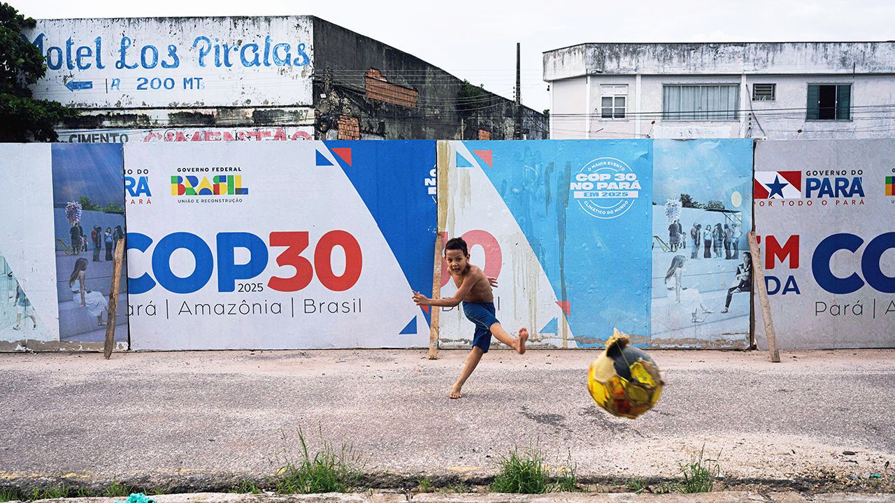 A boy kicks a soccer ball near signage for the COP30