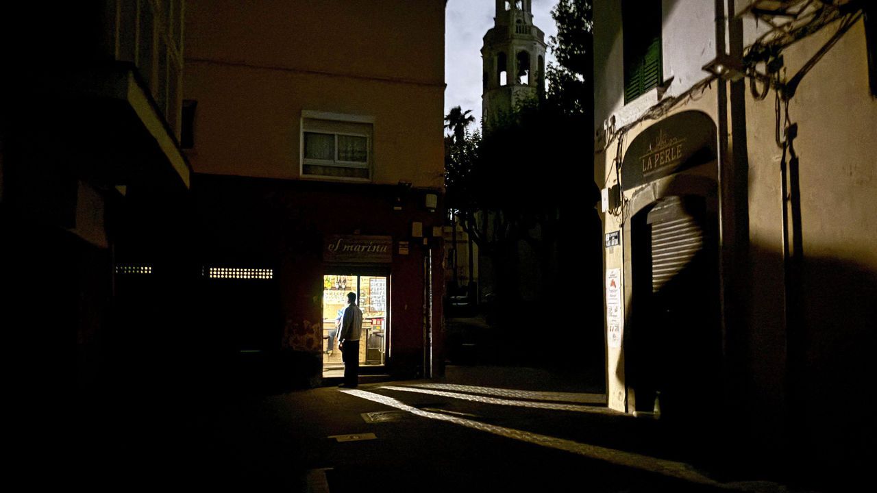A man stands in a corner pub lit by a camping lamp in the small town of Premia de Mar 