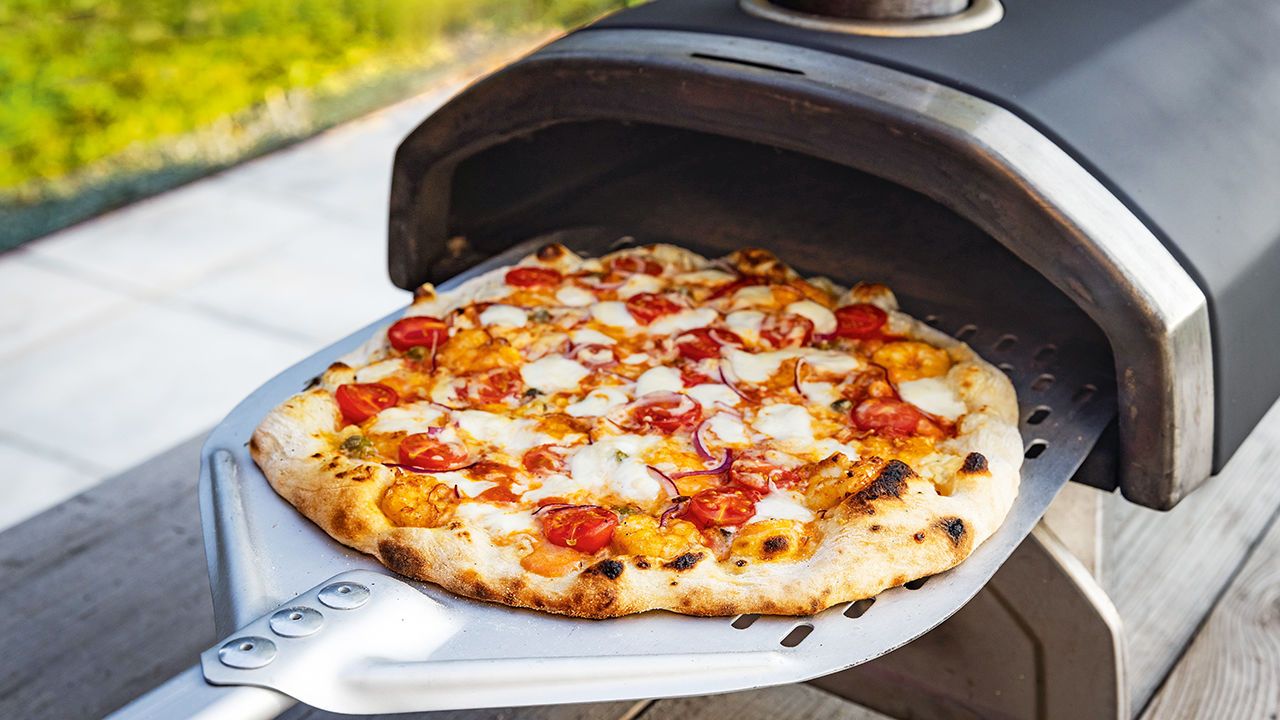 Pizza being taken out of a portable pizza oven