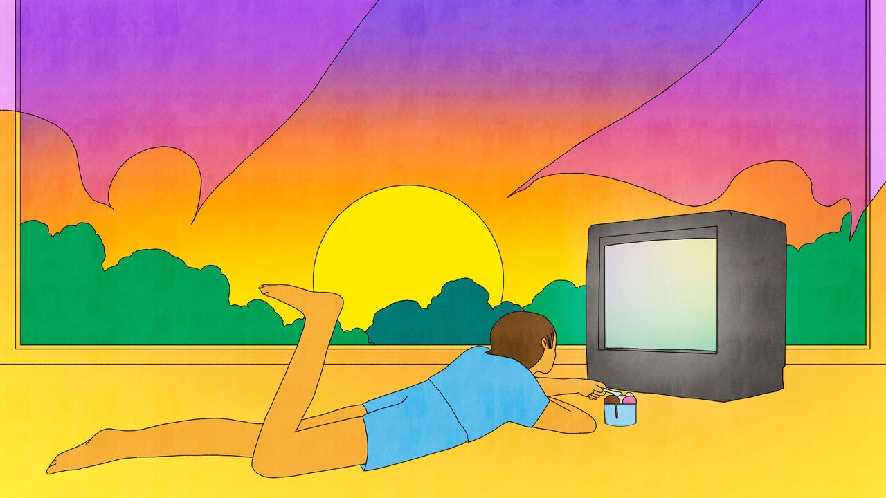 A person eats ice cream whilst lying in front of a television. The sunset can be seen through a large window
