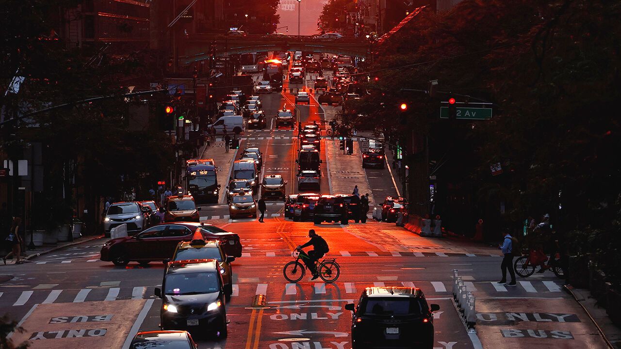 A cyclist crosses 42nd Street in front of traffic as the sun sets in New York City.