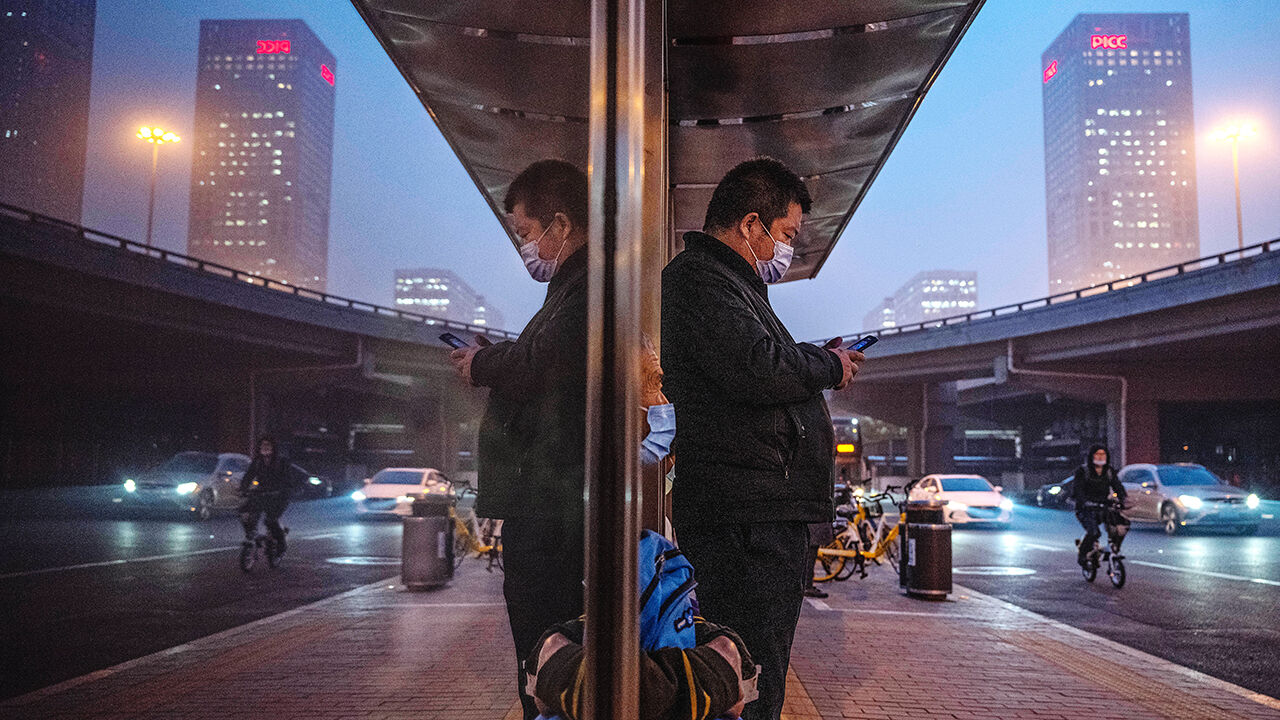 A man looks at his mobile phone while waiting for a bus in China.